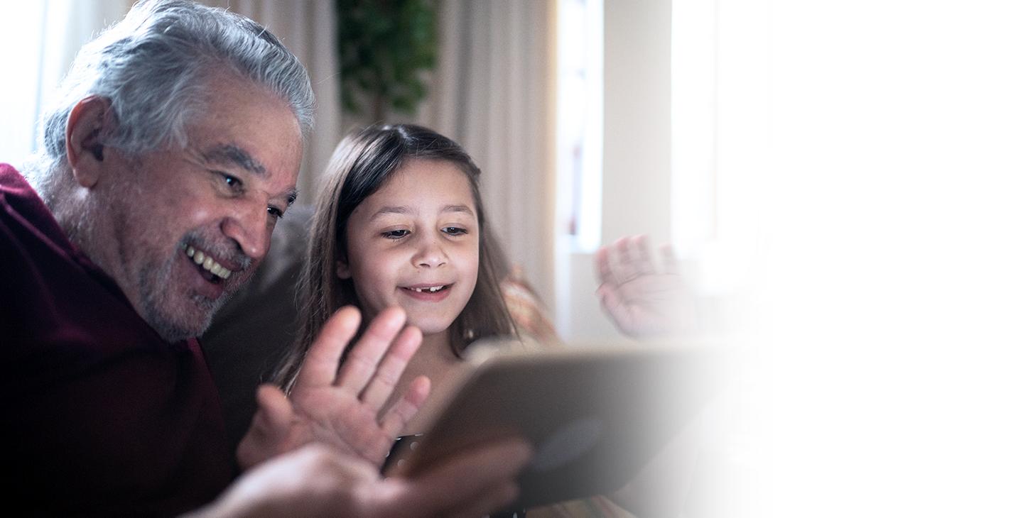 Child sitting with her grandfather staying connected to the internet on their tablet with help from the FCC's 负担得起的连接计划.